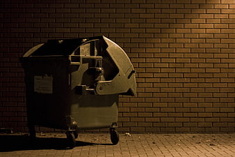 Old industrial waste container against brick wall at night