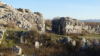 Ancient stone ruins in a grassy landscape with distant mountains