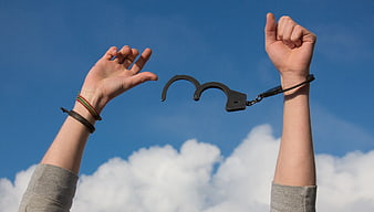 Freedom Concept: Hands Breaking Handcuffs Against Blue Sky