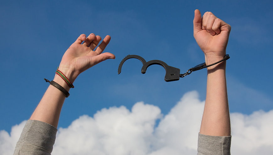 Freedom Concept: Hands Breaking Handcuffs Against Blue Sky