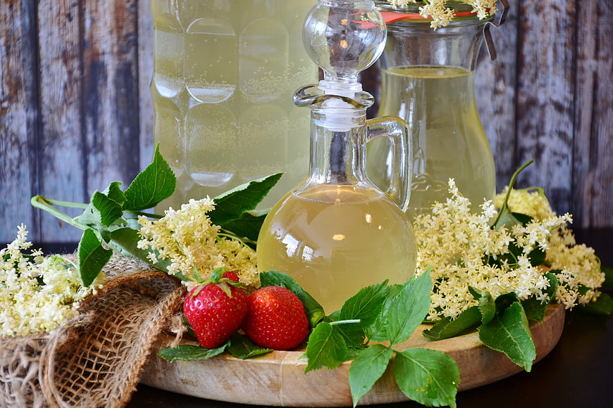 Elderflower syrup in glass bottles with fresh strawberries and blossoms