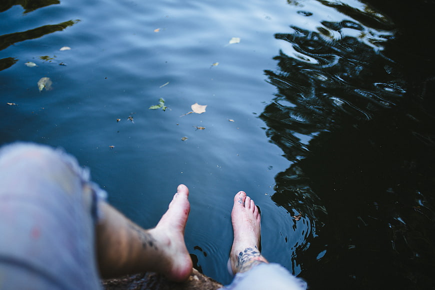 Relaxing bare feet with tattoos dipping in dark water