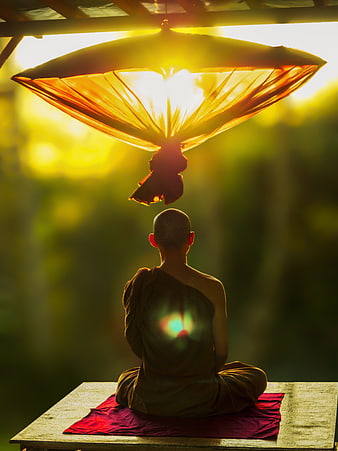 Buddhist monk meditating under a traditional umbrella at sunset