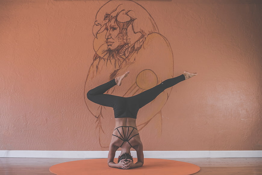 Woman performing headstand yoga pose in studio with mural