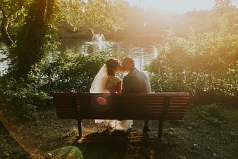 Romantic Wedding Couple Kissing on Park Bench by Lake