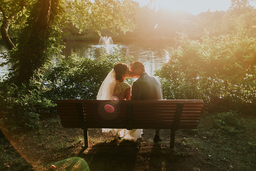 Romantic Wedding Couple Kissing on Park Bench by Lake