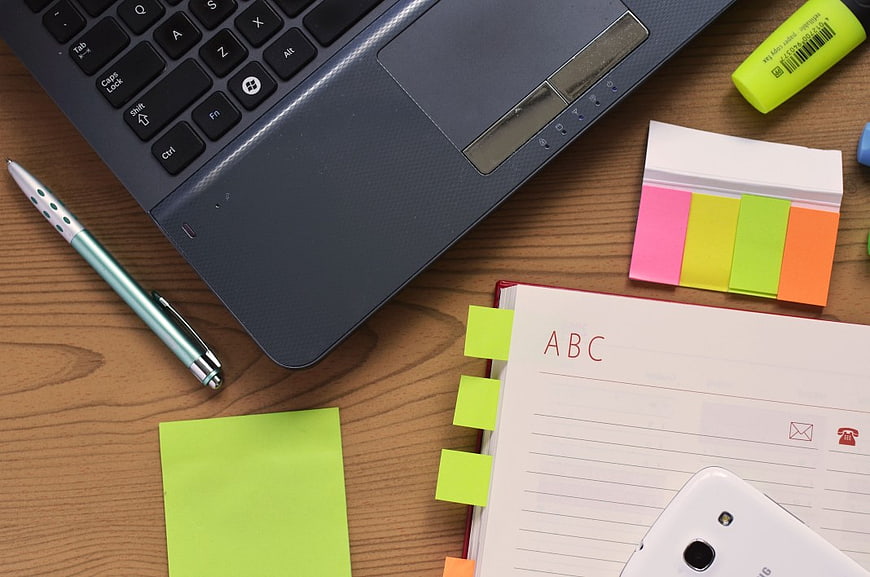 Top view of laptop, notebook, and office supplies on wooden desk