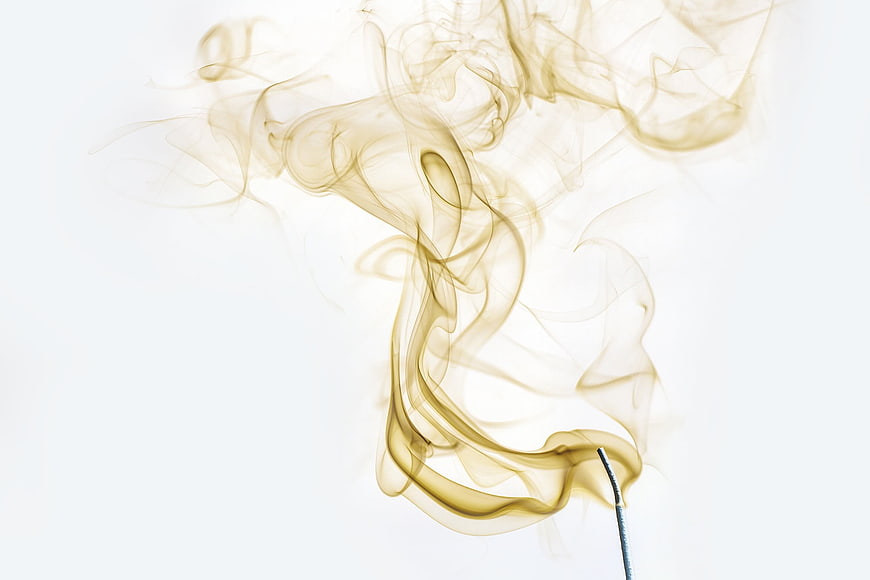 Golden incense smoke swirling on white background