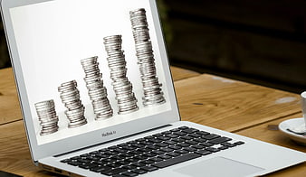 Laptop displaying coin stacks bar chart on wooden desk