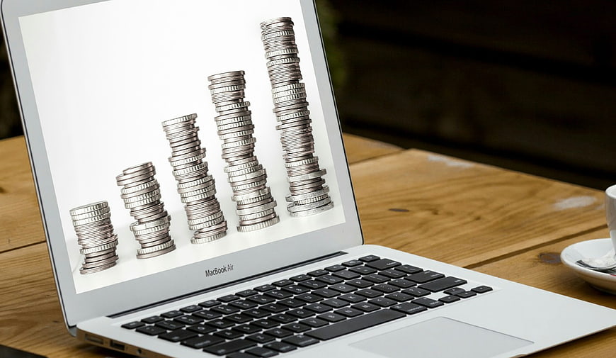 Laptop displaying coin stacks bar chart on wooden desk