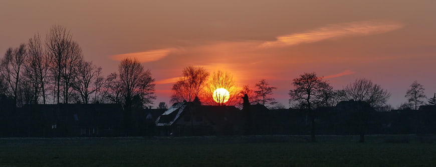 Panoramic sunset over rural landscape with silhouetted trees and houses