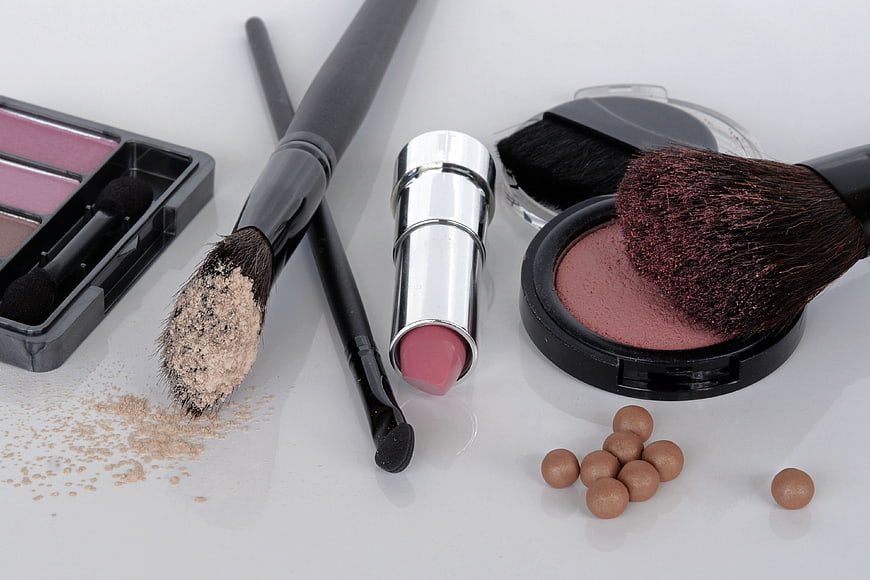 Flat lay of makeup brushes, lipstick, and powder on white background