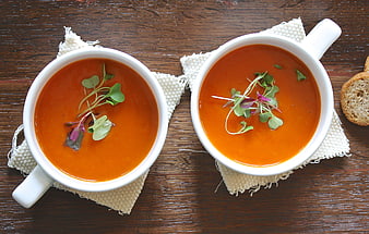 Overhead view of two bowls of orange soup with microgreens