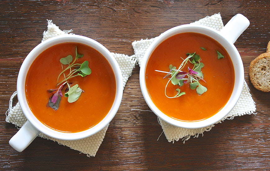Overhead view of two bowls of orange soup with microgreens