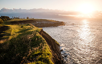 Golden sunset over grassy coastal cliffs and ocean waves