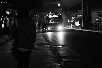 Woman Waiting for Bus on Wet City Street at Night