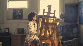 Young female artist painting on canvas in sunlit studio