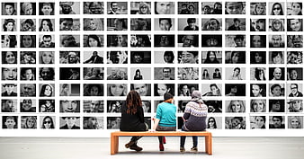 Three people sitting on bench viewing wall of black and white portraits