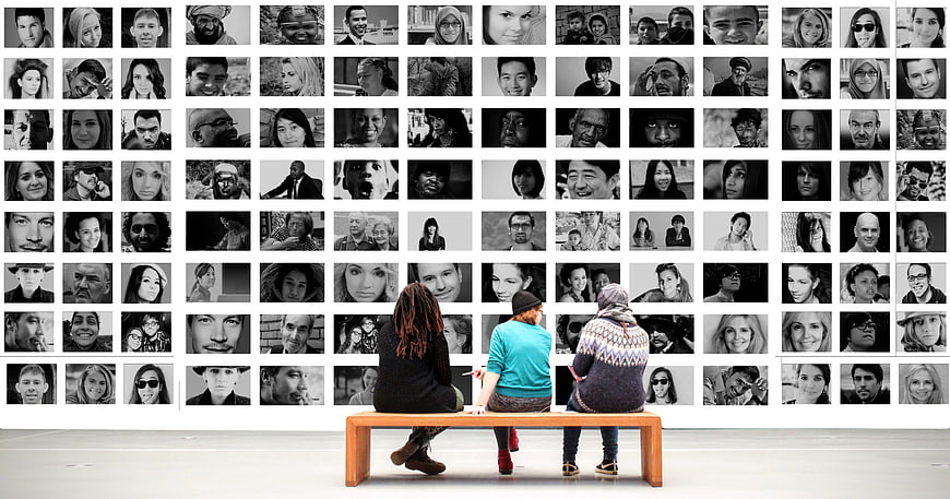 Three people sitting on bench viewing wall of black and white portraits