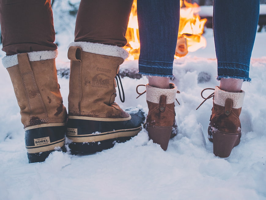 Couple's winter boots in snow near campfire