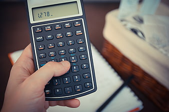 Hand holding financial calculator with money in background