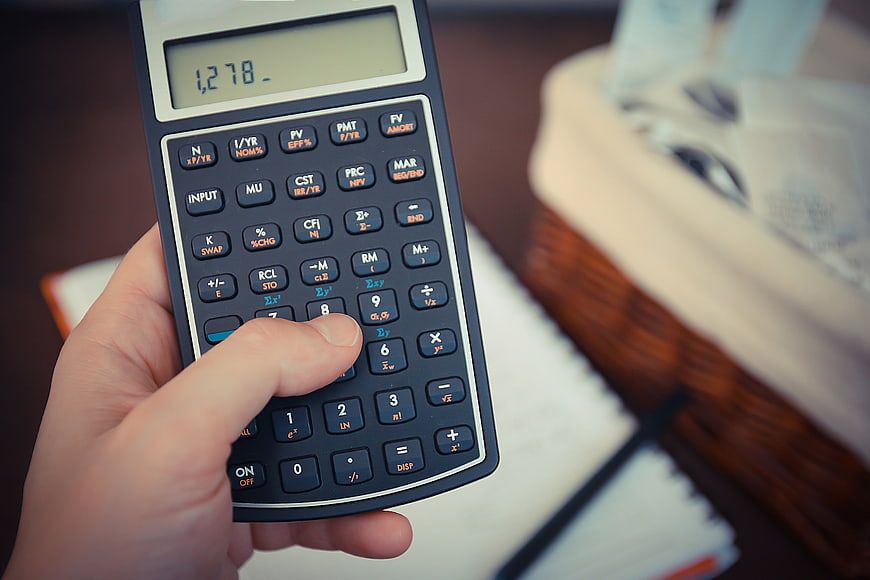 Hand holding financial calculator with money in background