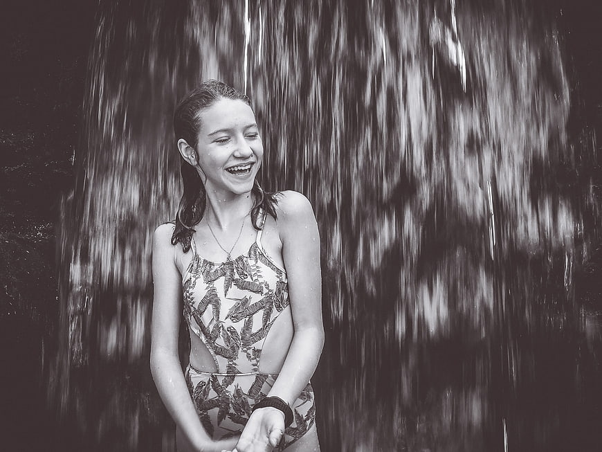 Laughing Girl in Swimsuit Under Waterfall