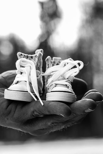 Baby sneakers held in weathered hand black and white