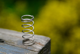 Metal coil spring on weathered wood with blurred green background