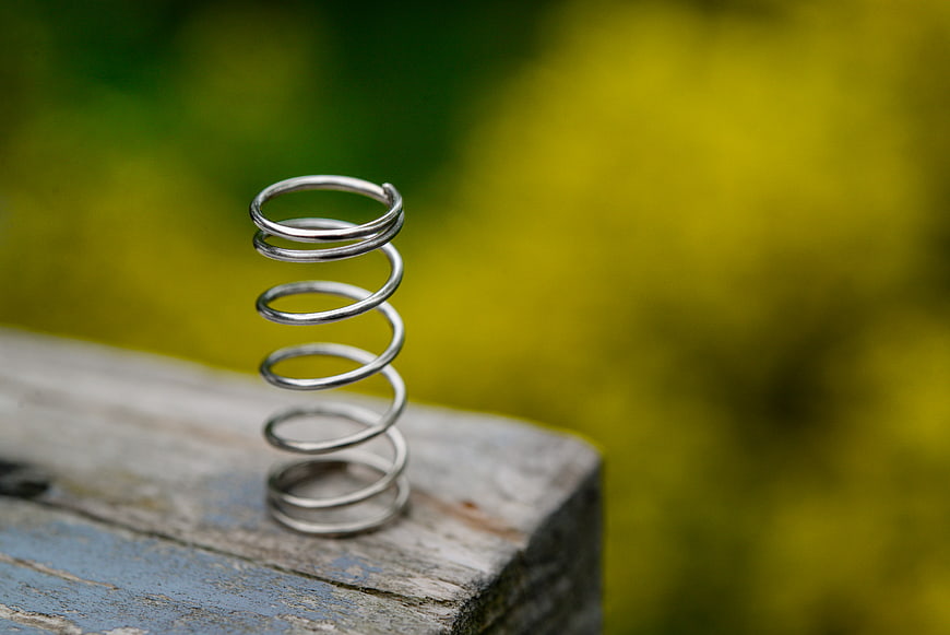 Metal coil spring on weathered wood with blurred green background
