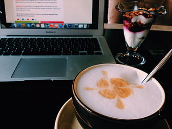 Latte with clover art and laptop on cafe table