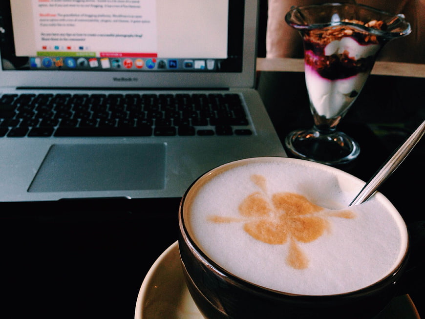 Latte with clover art and laptop on cafe table