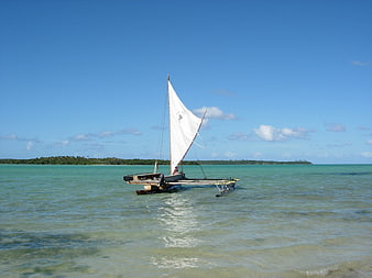 Traditional outrigger canoe with white sail on turquoise tropical lagoon