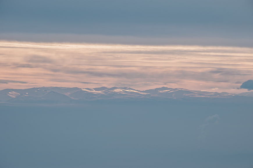 Snowy mountain peaks above clouds at sunset