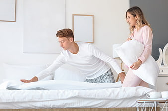 Young couple making bed together in bright bedroom