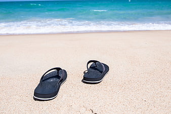 Black flip flops on sandy beach with ocean waves