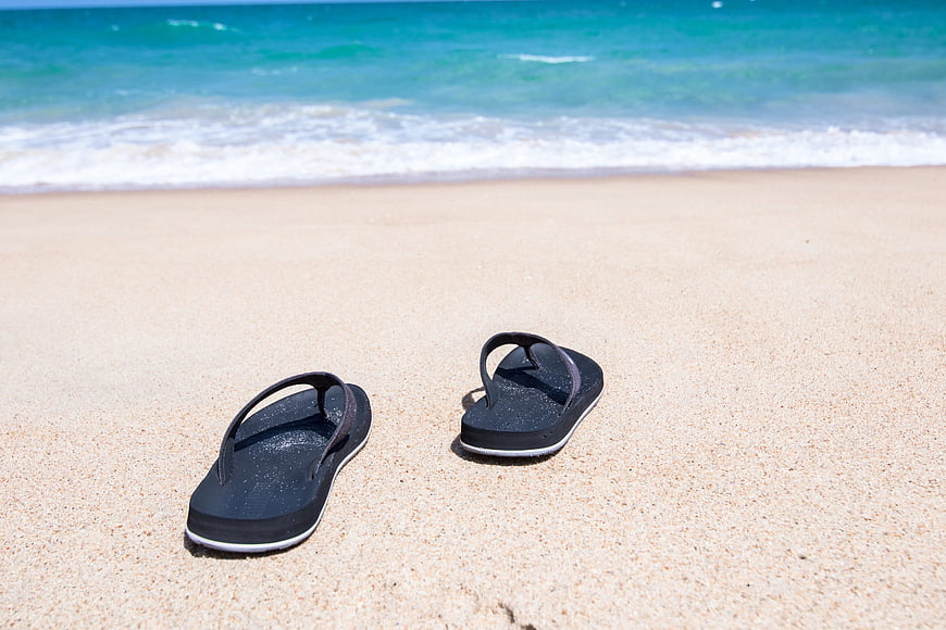 Black flip flops on sandy beach with ocean waves