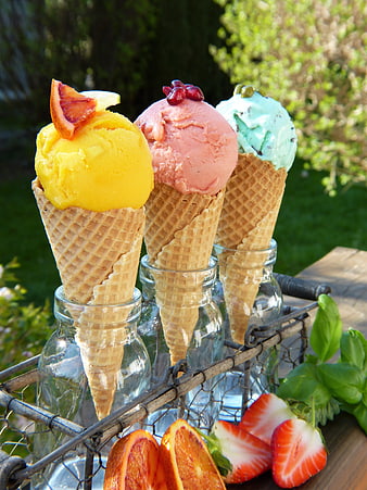 Three colorful fruit sorbet cones in glass bottles outdoors