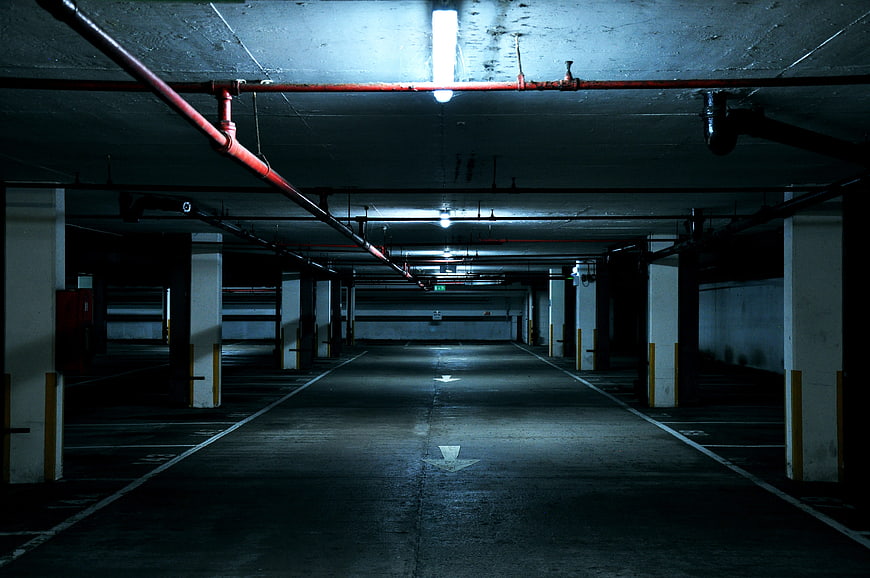 Empty Underground Parking Garage With Red Pipes And Concrete Pillars