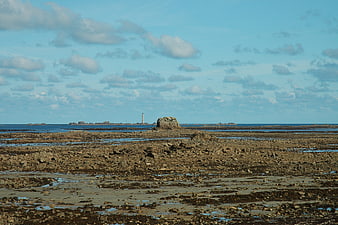 Rugged rocky coastline at low tide with distant lighthouse