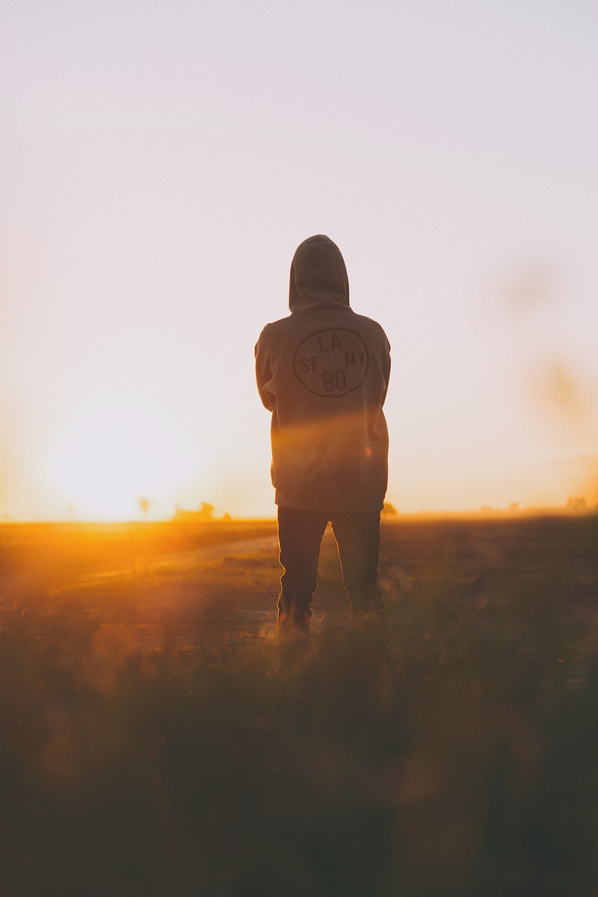 Silhouette of Man in Hoodie Standing in Field at Sunset