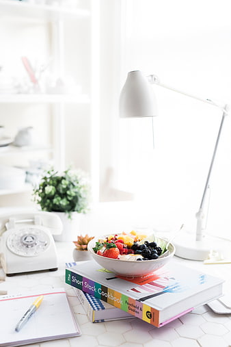 Healthy fruit bowl on stack of cookbooks in bright workspace