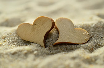 Two wooden hearts resting on sandy beach texture