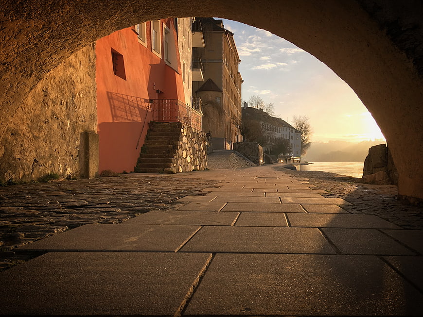 Sunlit cobblestone path under stone archway by river