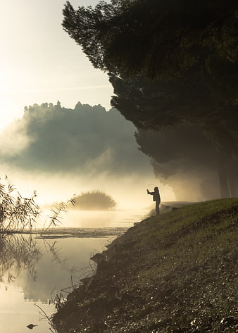 Silhouette of Fly Fisherman on Misty Riverbank at Sunrise