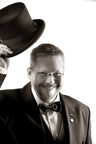 Smiling man in tuxedo tipping top hat in black and white