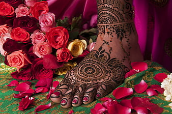 Close-up of Indian bride's foot with intricate henna mehndi design and red roses