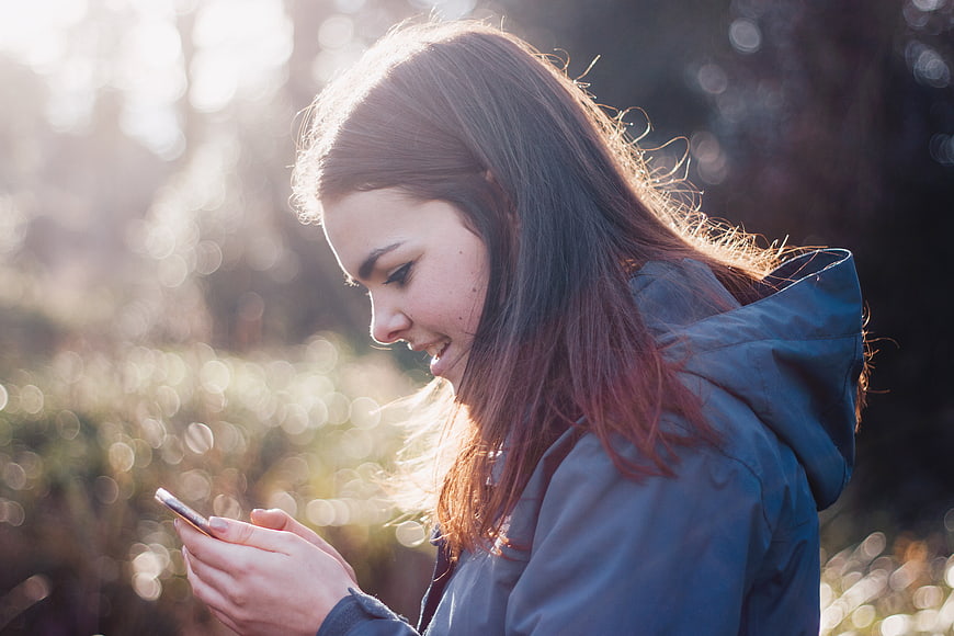 Young Woman Smiling at Smartphone in Sunlit Park