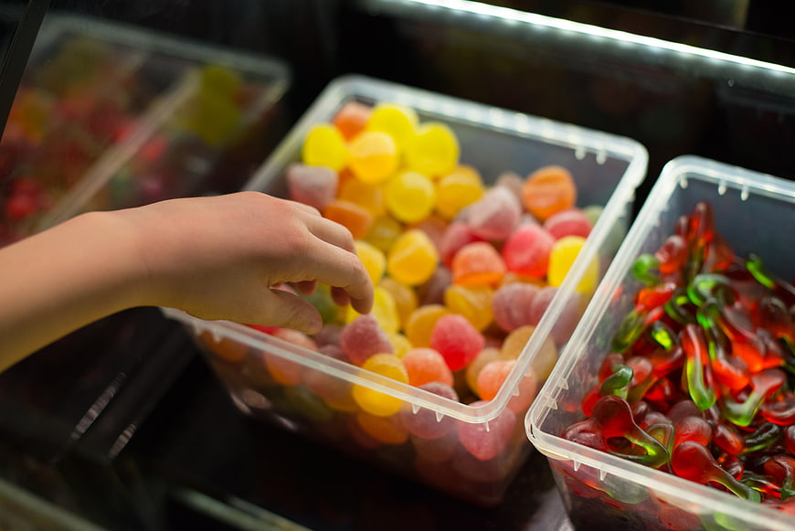 Child's hand picking colorful gummy candies from plastic bins
