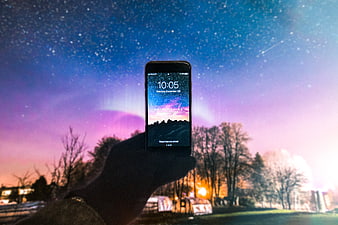 Hand holding smartphone with starry night sky wallpaper